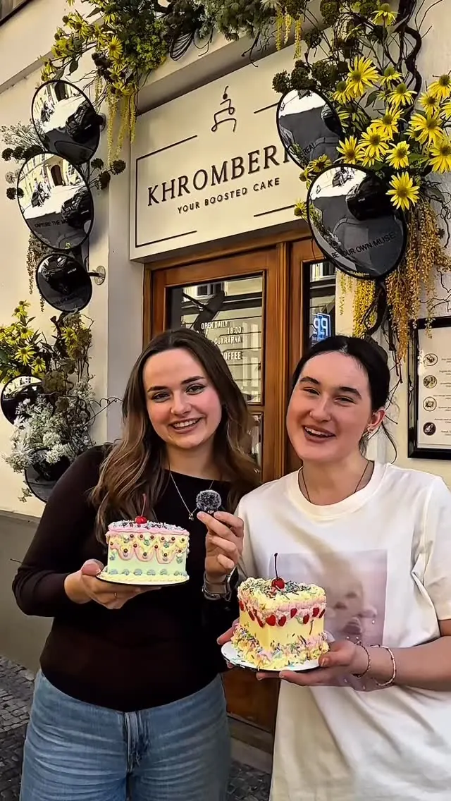 Two smiling team members holding pastel vintage-style cakes in front of the Khromberry storefront